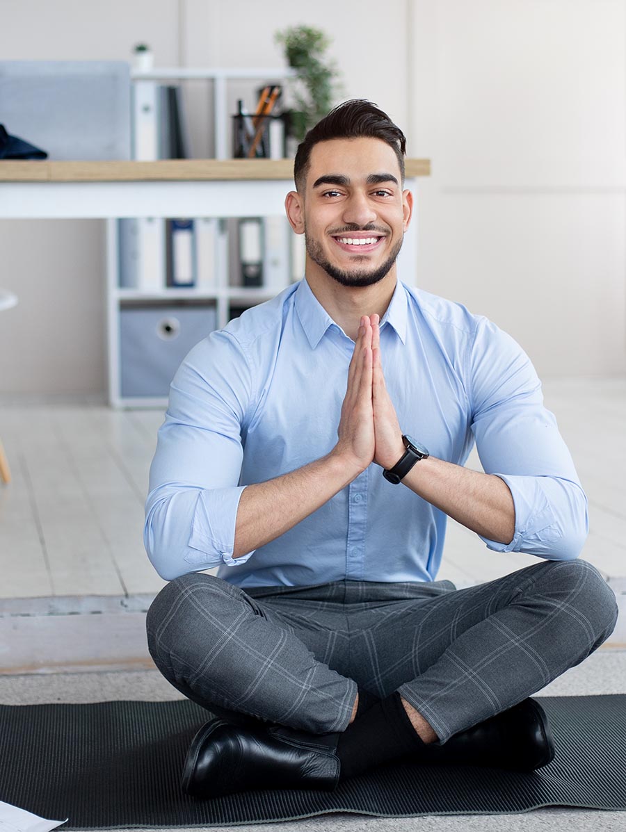 Workplace stress management. Peaceful Arab employee meditating, making namaste gesture on yoga mat at office